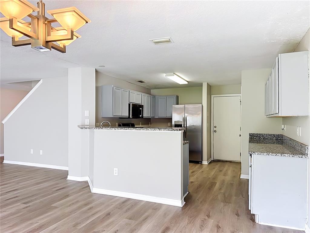 A kitchen with gray cabinets, granite countertops, and stainless steel appliances overlooks a living area — 6320 MAGNOLIA TRAILS LANE, GIBSONTON, FL