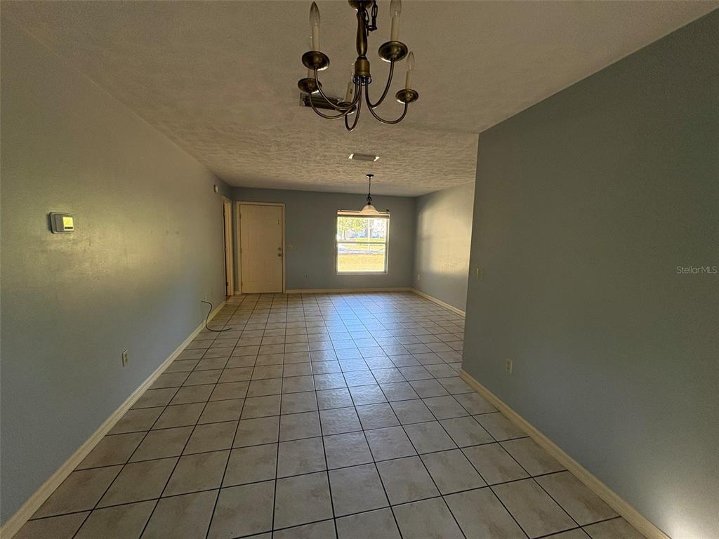 A long, tiled room features a chandelier, a window, and a light-colored door — 2060 NW 42ND STREET, OCALA, FL