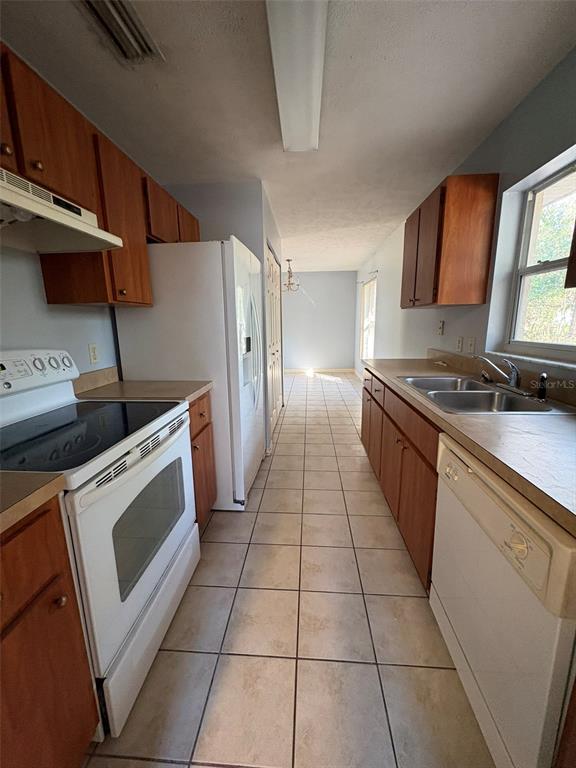 A galley-style kitchen features wood cabinets, white appliances, tile flooring, and a double sink — 2060 NW 42ND STREET, OCALA, FL
