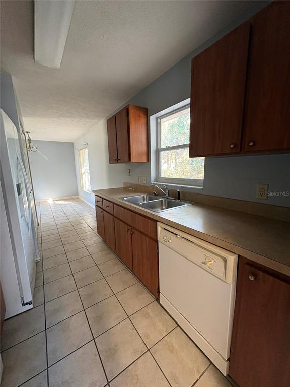 A kitchen features wood cabinets, a white dishwasher, a double sink, and tiled flooring — 2060 NW 42ND STREET, OCALA, FL