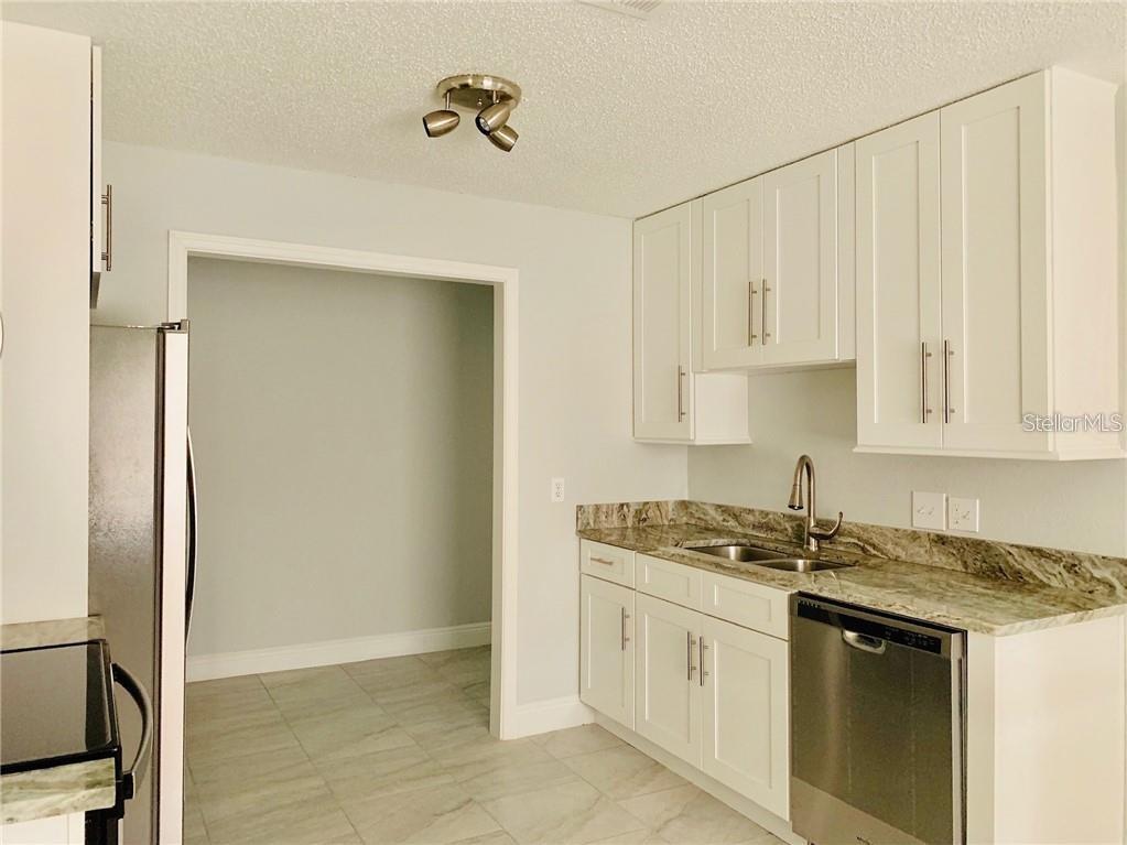 A kitchen features white cabinets, granite countertops, stainless steel appliances, and light tile flooring — 205 BABSON DRIVE, BABSON PARK, FL