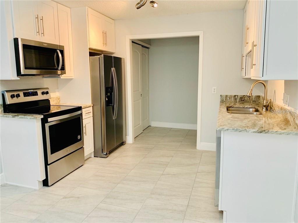 A kitchen features white cabinets, stainless steel appliances, and light-colored granite countertops — 205 BABSON DRIVE, BABSON PARK, FL