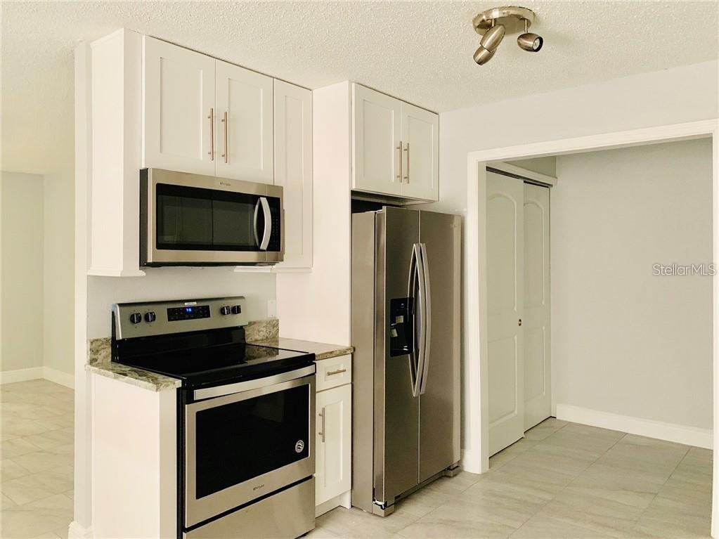 A kitchen features white cabinets, stainless steel appliances, and light-colored tile flooring — 205 BABSON DRIVE, BABSON PARK, FL