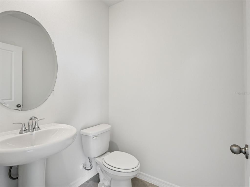 A small bathroom features a white pedestal sink, a round mirror, and a white toilet — 11329 BELLEWOOD TERRACE, PARRISH, FL