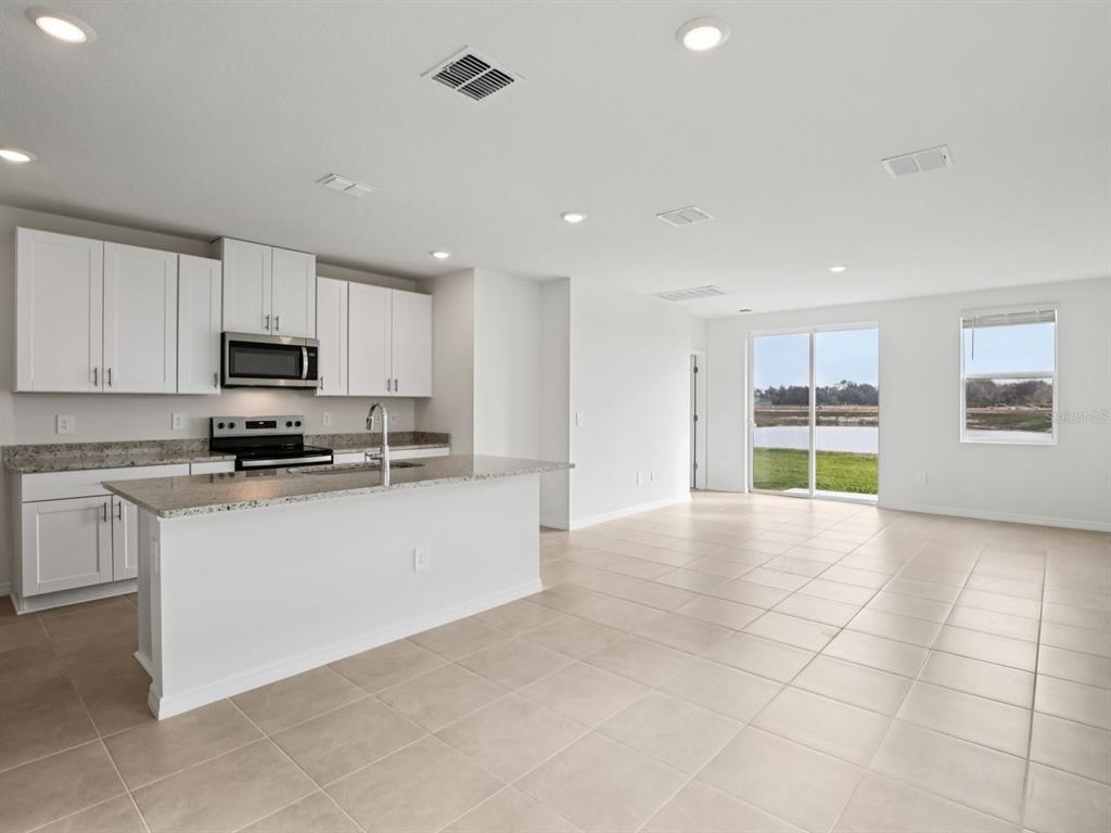 A kitchen with white cabinets and a granite island opens to a tiled living area — 11329 BELLEWOOD TERRACE, PARRISH, FL