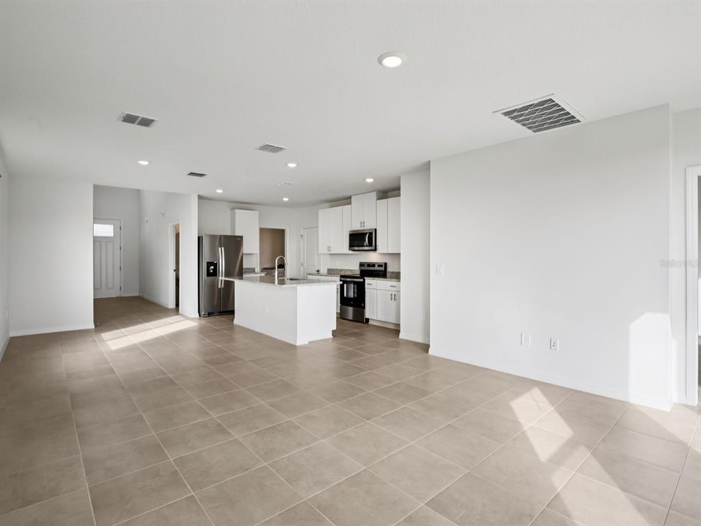 An open-concept kitchen and living area features white cabinets, stainless steel appliances, and tile flooring — 11329 BELLEWOOD TERRACE, PARRISH, FL