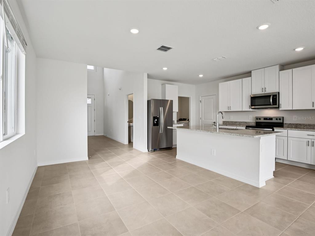 A modern kitchen features white cabinets, stainless steel appliances, and a granite-topped island — 11329 BELLEWOOD TERRACE, PARRISH, FL