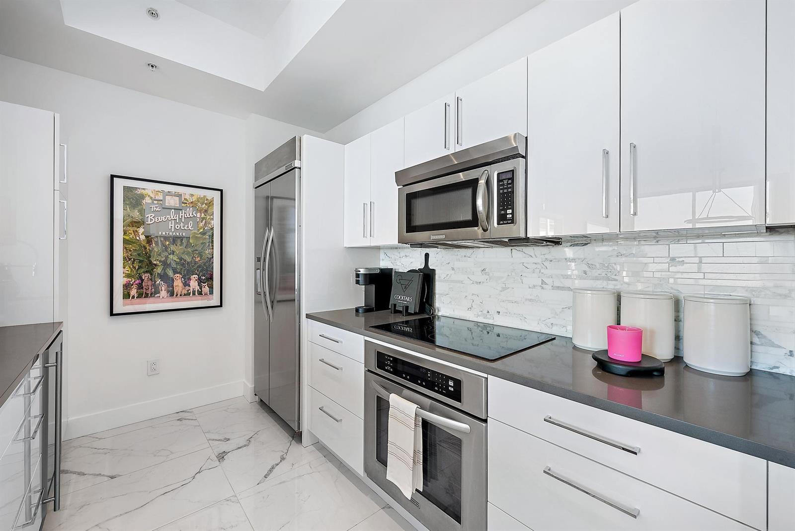A modern kitchen features white cabinets, stainless steel appliances, marble-style flooring, and a framed wall print — 550 Okeechobee Boulevard # 03, West Palm Beach FL 33401, WEST PALM BEACH, FL