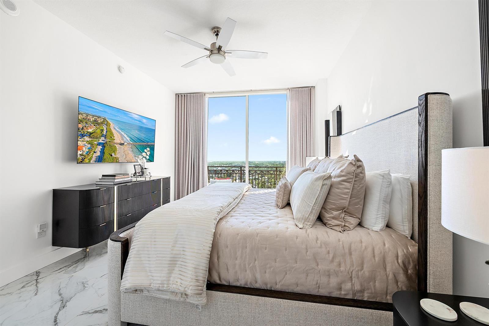 A bedroom with a king bed, marble floors, a wall-mounted television, and a balcony view — 550 Okeechobee Boulevard # 03, West Palm Beach FL 33401, WEST PALM BEACH, FL
