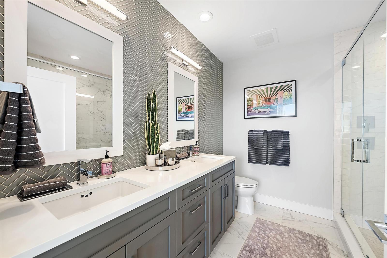 A bathroom features a double vanity with gray cabinets, a herringbone tile wall, and shower — 550 Okeechobee Boulevard # 03, West Palm Beach FL 33401, WEST PALM BEACH, FL