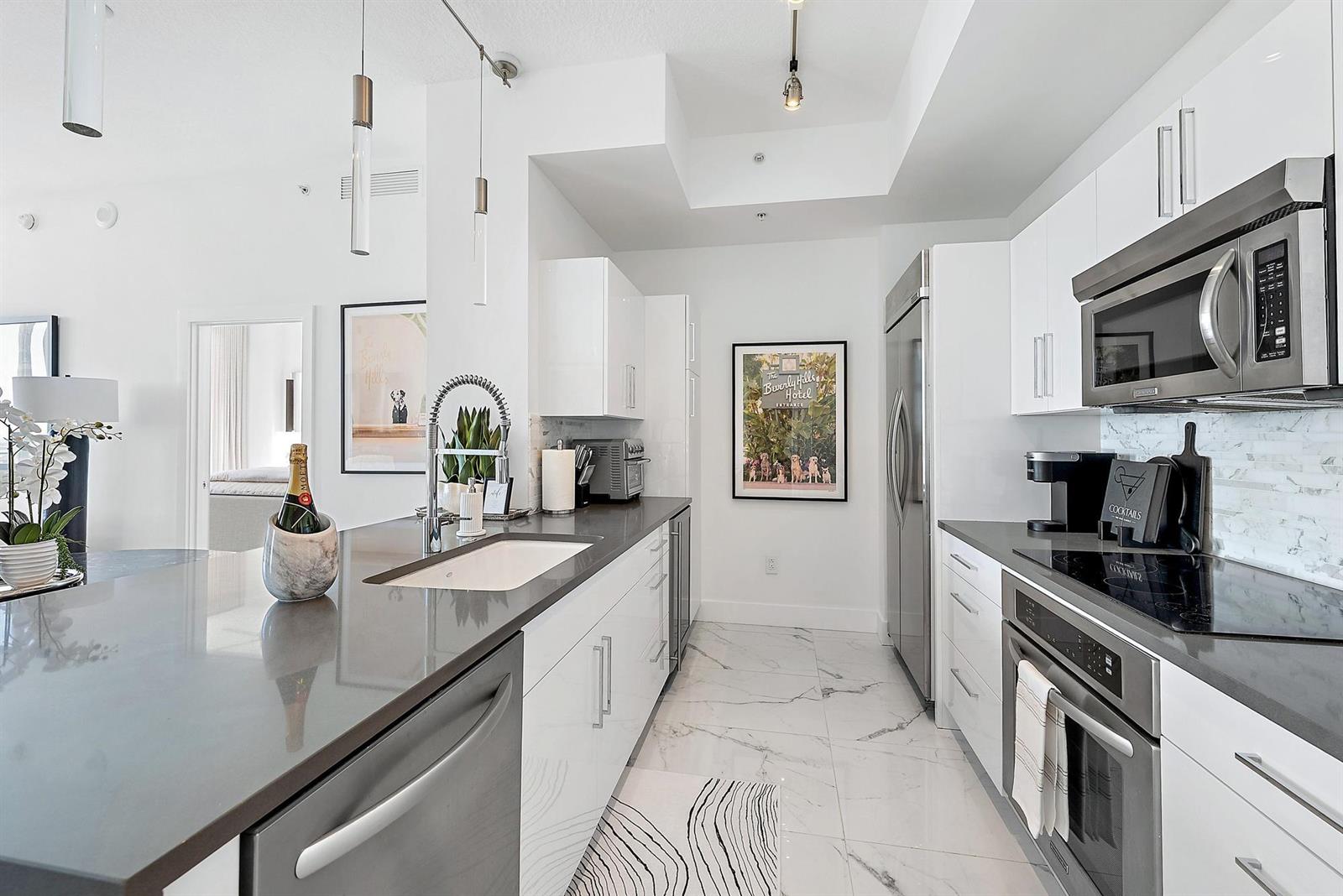 A modern kitchen features white cabinets, dark countertops, stainless steel appliances, and marble-style tile flooring — 550 Okeechobee Boulevard # 03, West Palm Beach FL 33401, WEST PALM BEACH, FL