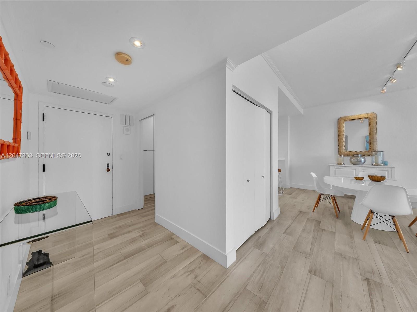 An entryway with light wood flooring leads to a dining area with white furniture — KEY BISCAYNE, FL