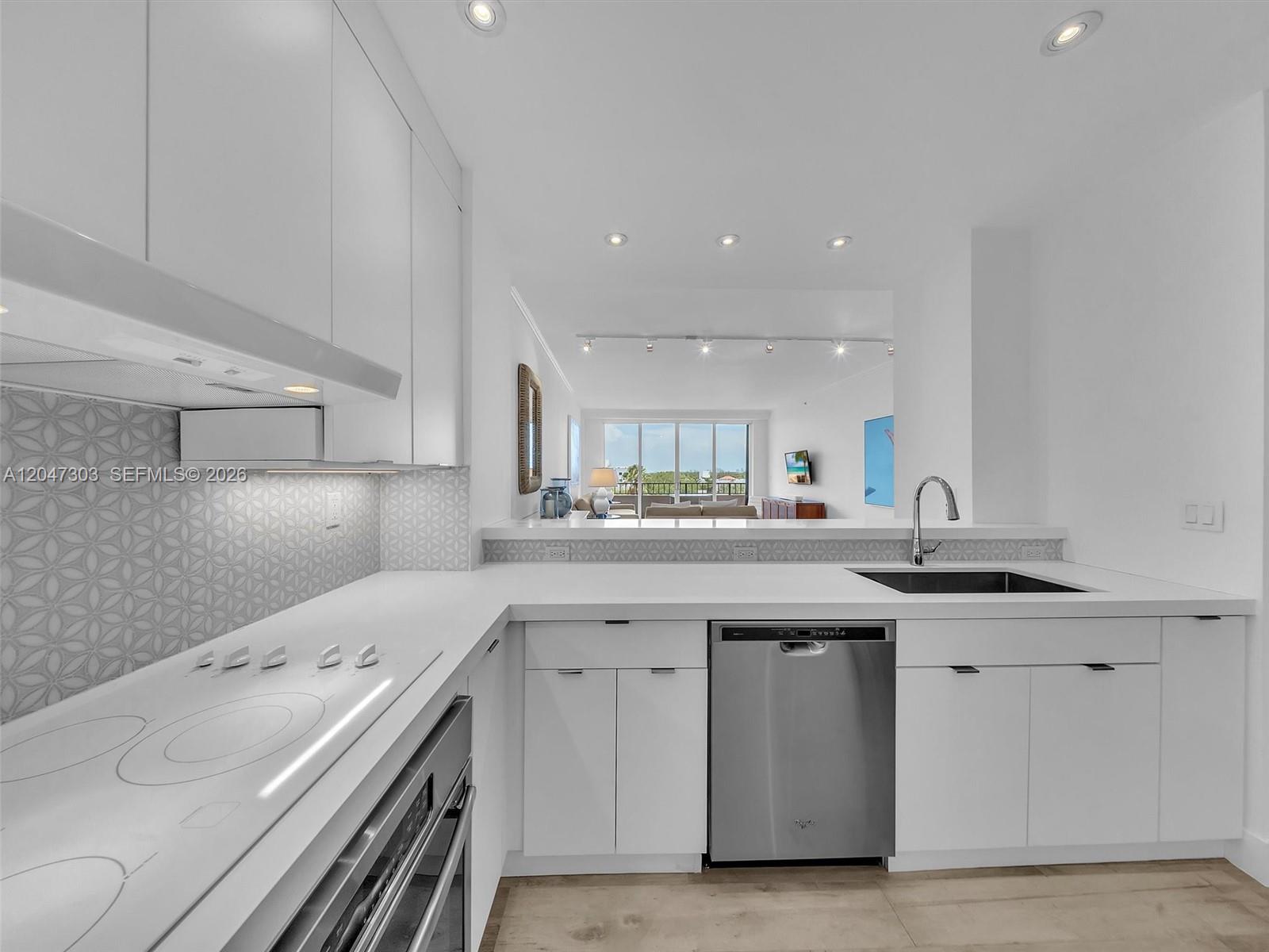 A modern white kitchen features a stainless steel dishwasher, electric cooktop, and patterned backsplash — KEY BISCAYNE, FL