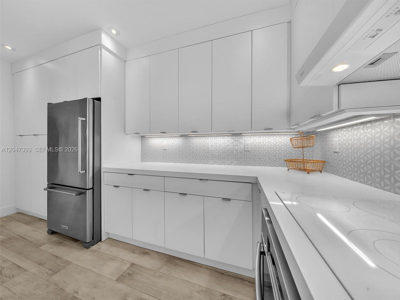 A modern kitchen features white flat-panel cabinetry, a stainless steel refrigerator, and a patterned backsplash — KEY BISCAYNE, FL