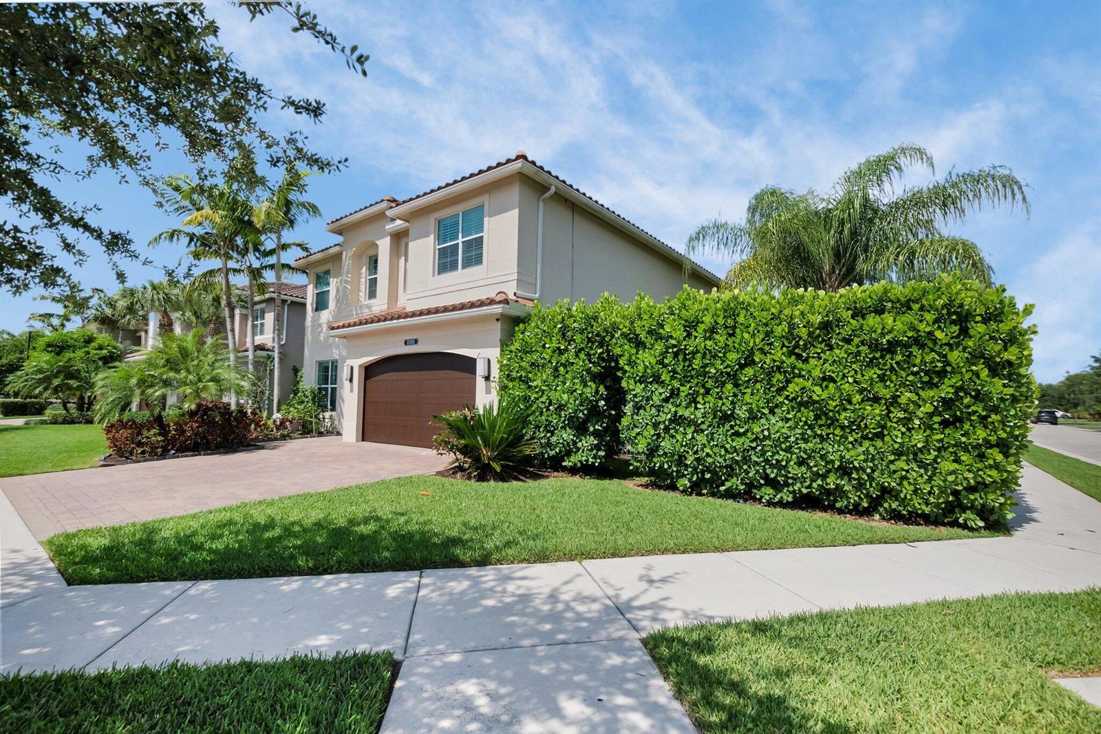 A two-story beige house with a brown garage door and a large green privacy hedge — 15205 Seaglass Terrace Lane, Delray Beach FL 33446, DELRAY BEACH, FL