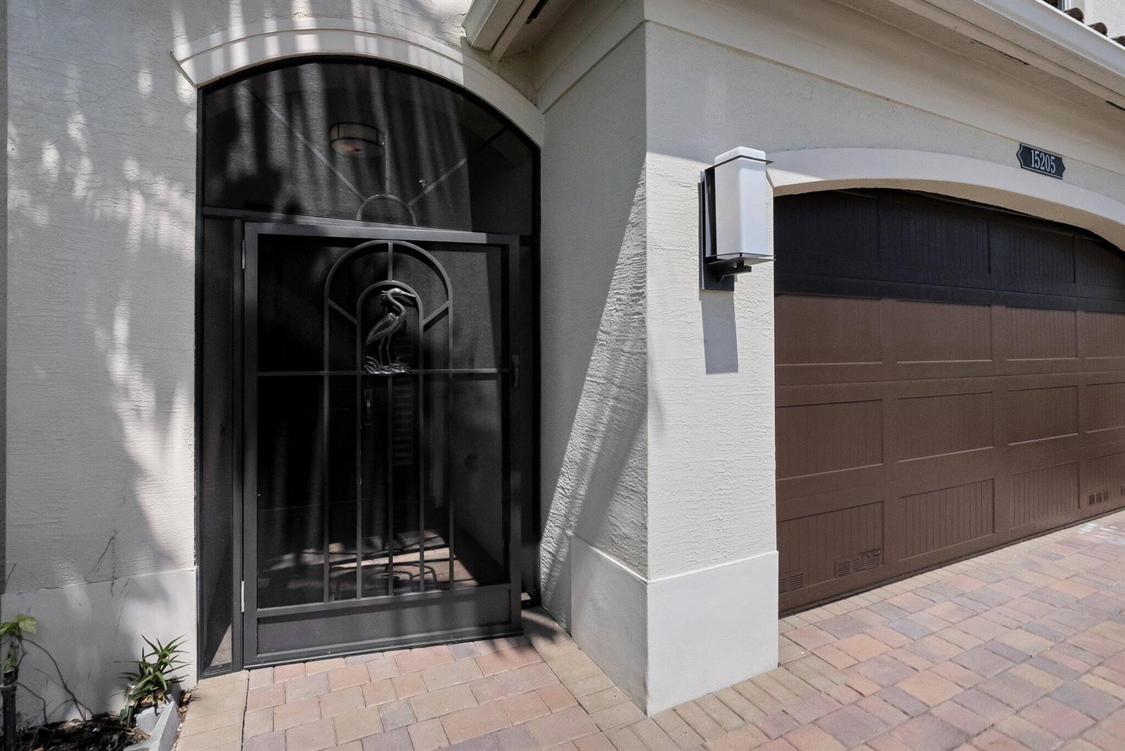 A dark metal screen door with a heron design sits beside a brown garage door — 15205 Seaglass Terrace Lane, Delray Beach FL 33446, DELRAY BEACH, FL