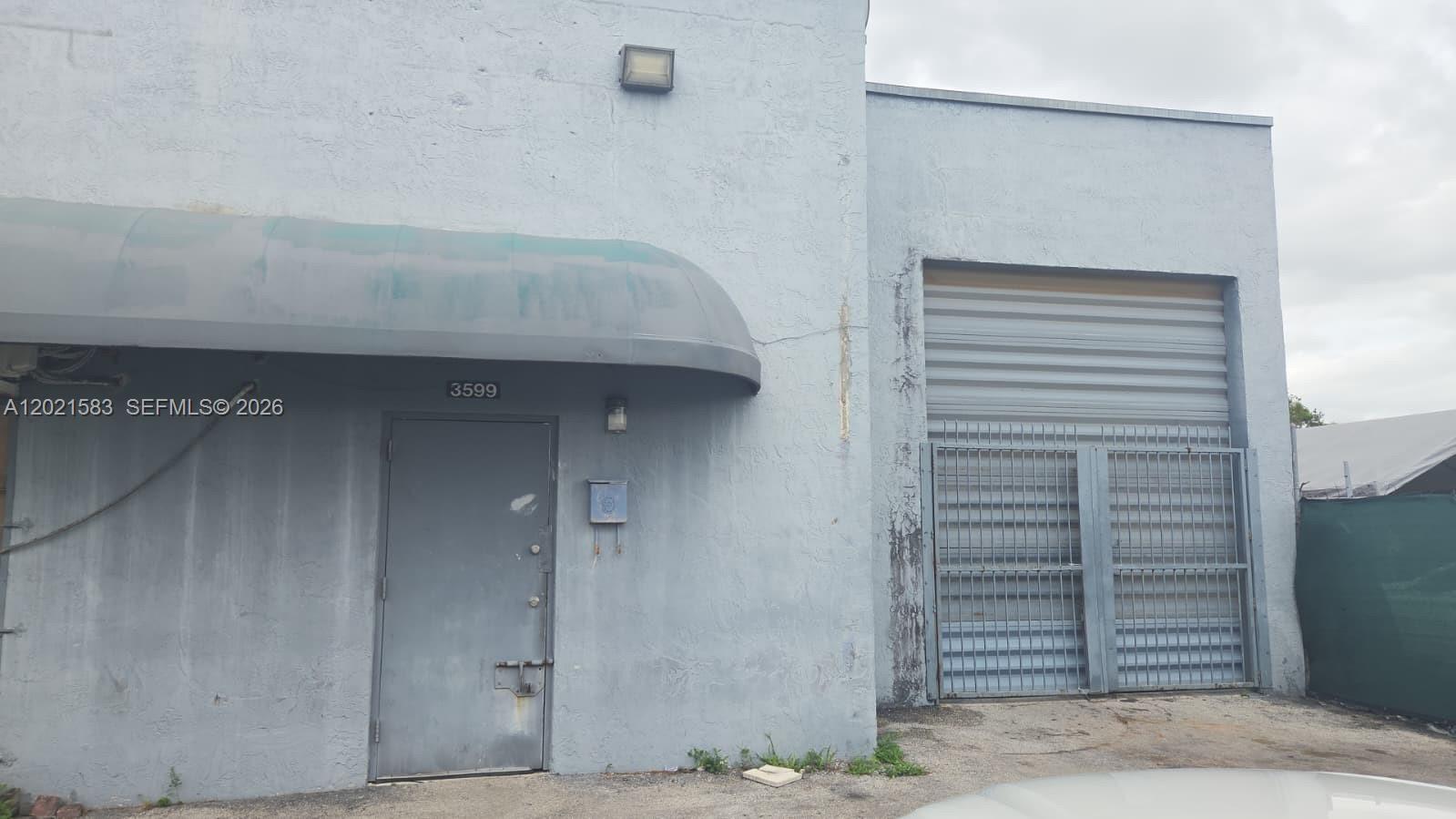 The exterior of a light blue industrial building features a metal door and a roll-up gate — 3585 NW 154th Ter, Miami Gardens FL 33054, MIAMI GARDENS, FL