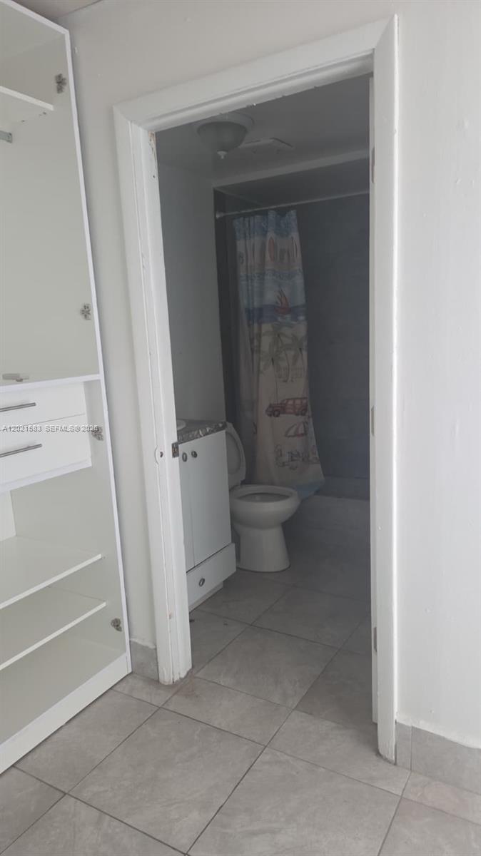 A view through a doorway into a bathroom with a toilet and shower curtain — 3585 NW 154th Ter, Miami Gardens FL 33054, MIAMI GARDENS, FL
