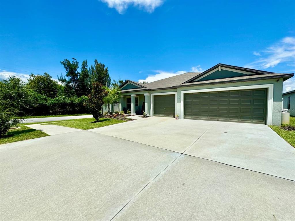 A single-story house with a three-car garage and a concrete driveway under a blue sky — 1881 SAND DAISY PLACE, RUSKIN, FL