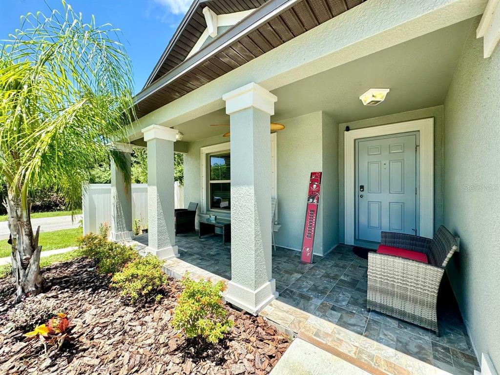 A covered front porch features tiled flooring, square columns, and a light blue front door — 1881 SAND DAISY PLACE, RUSKIN, FL