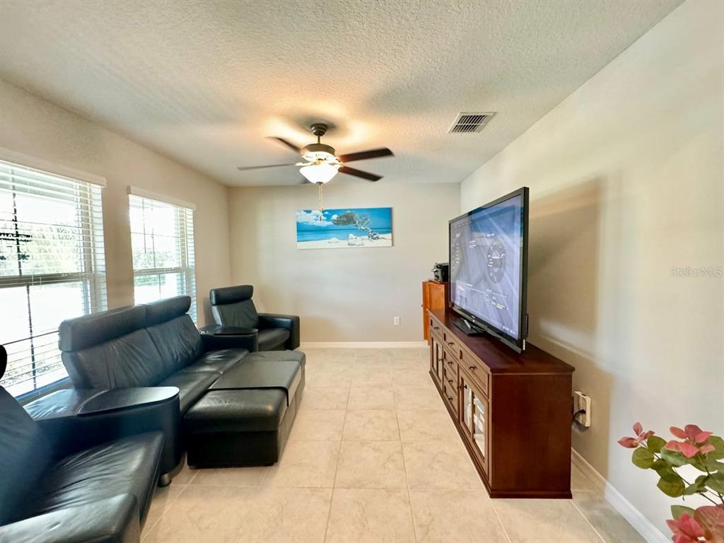 A living room features tile flooring, a ceiling fan, black leather seating, and a television — 1881 SAND DAISY PLACE, RUSKIN, FL
