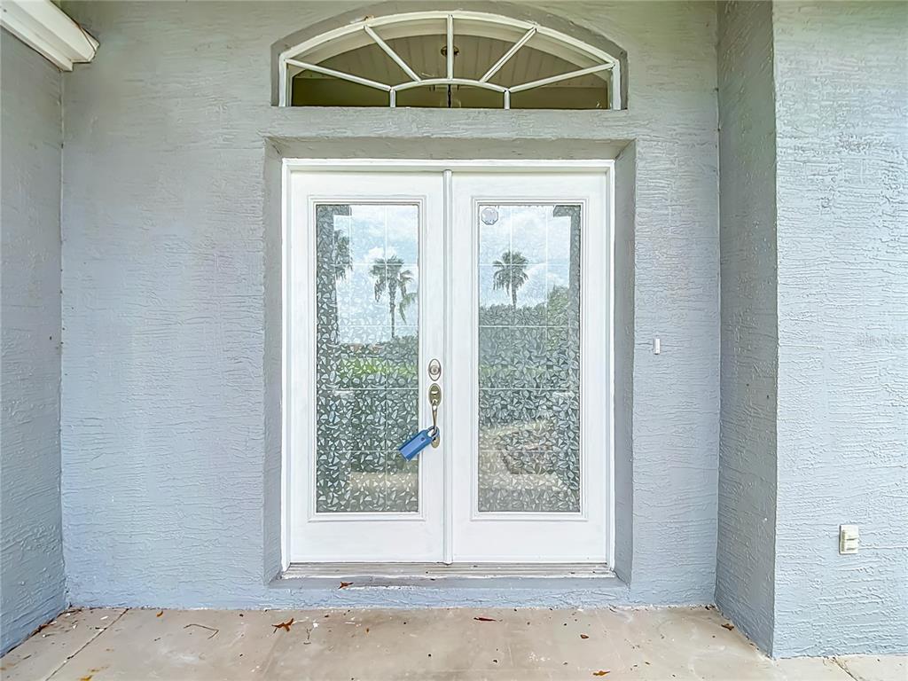 A gray exterior wall features a white double door with decorative glass and a transom window — 13827 WOODWARD DRIVE, HUDSON, FL