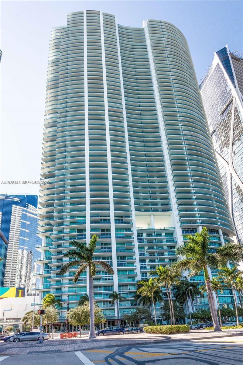 A tall, modern residential skyscraper with numerous balconies stands above palm trees and a street — 900 Biscayne Blvd # 2604, Miami FL 33132, MIAMI, FL
