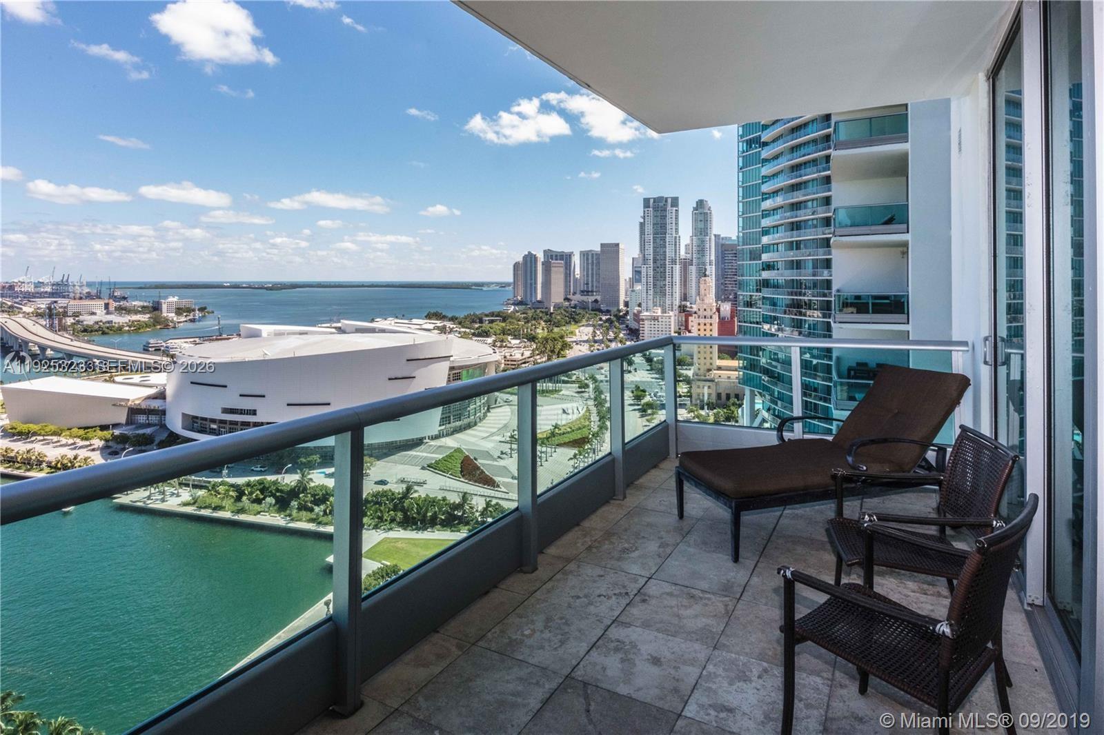 A balcony with outdoor furniture overlooks a city skyline, a large arena, and the water — 900 Biscayne Blvd # 2604, Miami FL 33132, MIAMI, FL