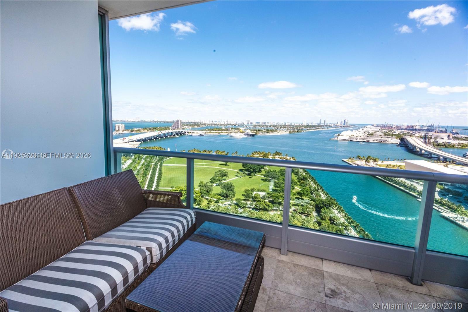 A balcony with outdoor furniture overlooks a park, a bridge, and a body of water — 900 Biscayne Blvd # 2604, Miami FL 33132, MIAMI, FL