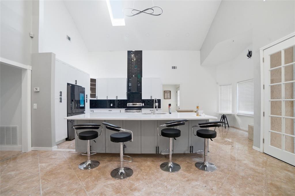 A modern kitchen features a large gray island, white cabinetry, black tile backsplash, and vaulted ceilings — 2054 PALM VISTA DRIVE, APOPKA, FL