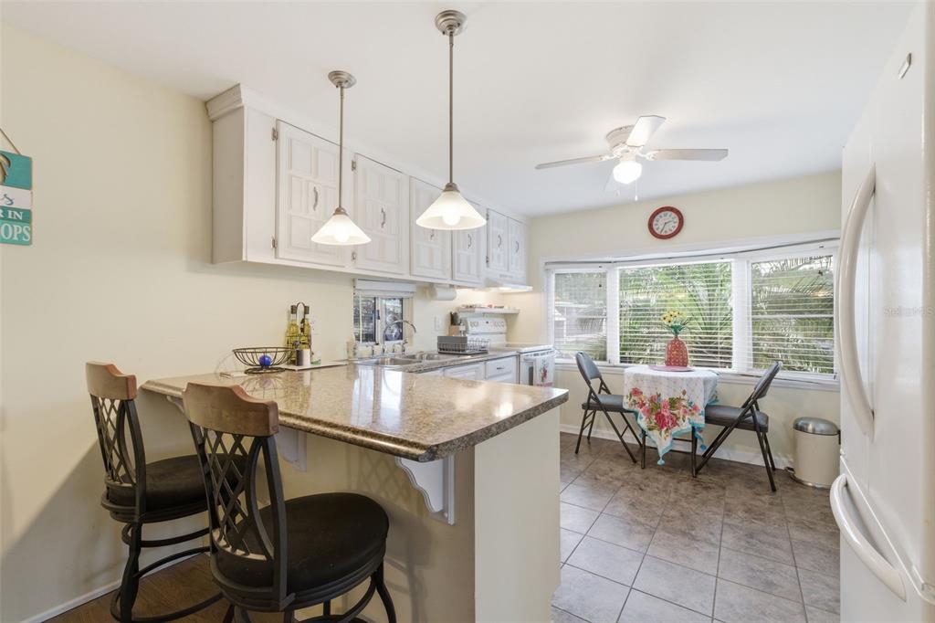 A kitchen features white cabinets, a granite breakfast bar, tile flooring, and a dining nook — 6100 62ND AVENUE N UNIT 38, PINELLAS PARK, FL