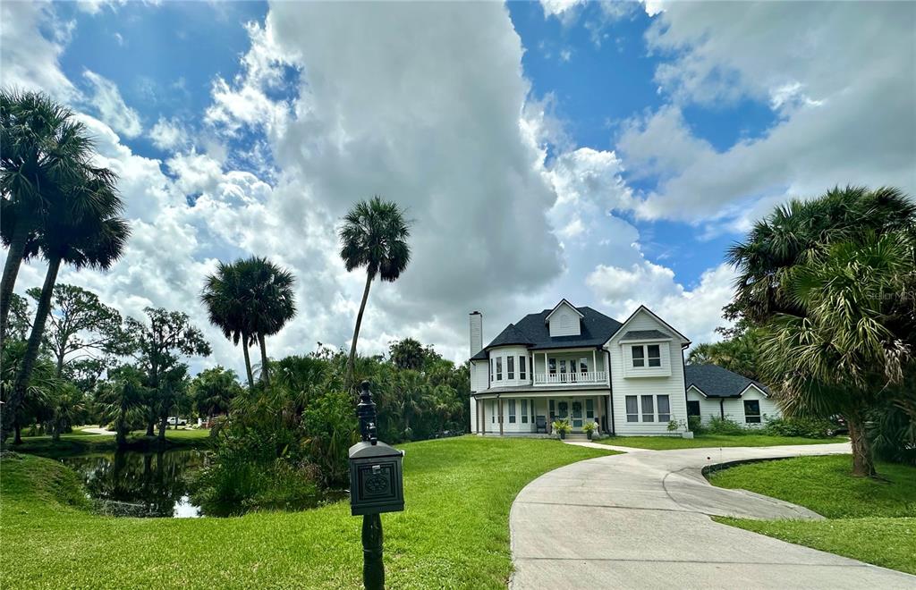 A two-story white house with a wrap-around porch sits behind a curved concrete driveway — 1587 FIRETHORNE LAKES DRIVE, SARASOTA, FL