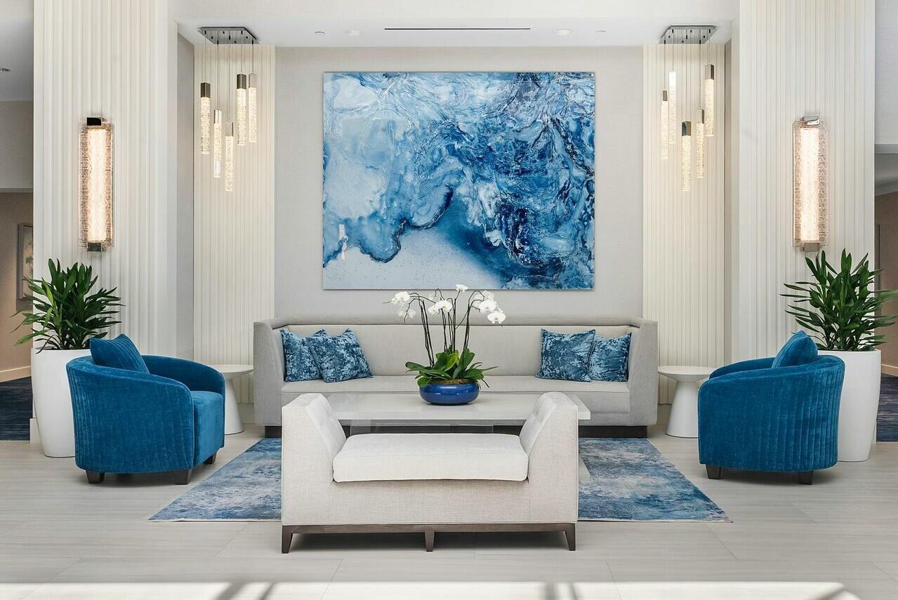 A modern lobby seating area features a blue abstract painting, a gray sofa, and blue armchairs — 4356 Kasso Circle, Boca Raton FL 33487, BOCA RATON, FL