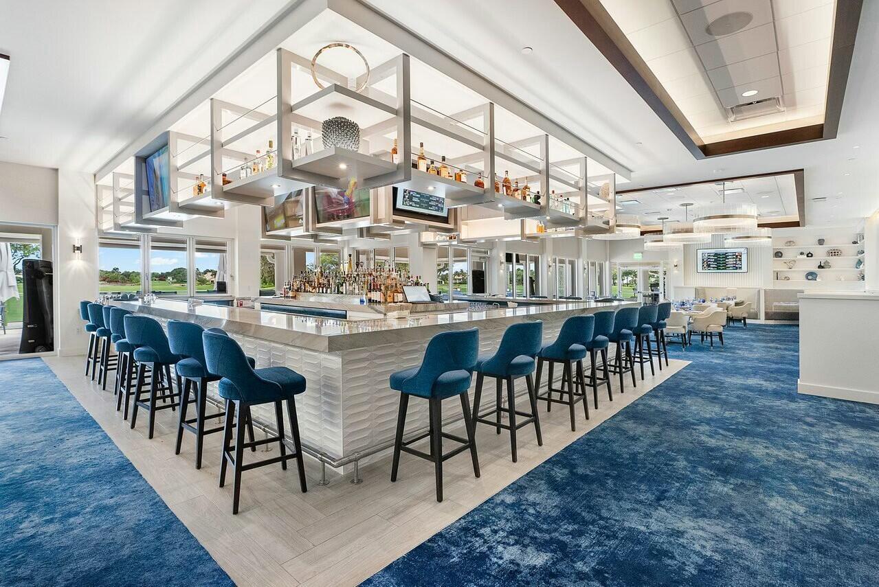 A modern bar area features blue upholstered stools, a white textured counter, and overhead shelving — 4356 Kasso Circle, Boca Raton FL 33487, BOCA RATON, FL