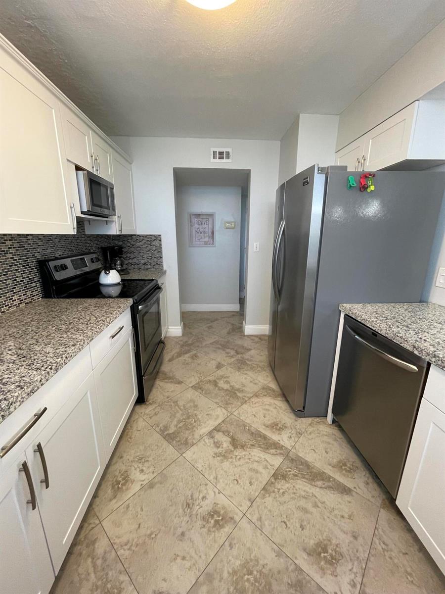 A galley kitchen features white cabinets, granite countertops, stainless steel appliances, and tiled flooring — 955 Dotterel Road # 2511, Delray Beach FL 33444, DELRAY BEACH, FL