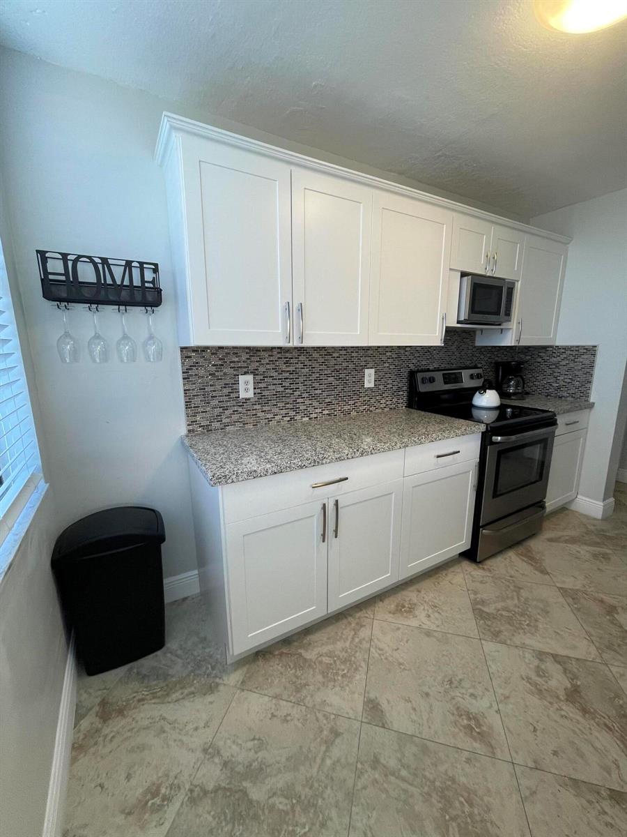 A kitchen features white cabinets, granite countertops, a mosaic tile backsplash, and stainless steel appliances — 955 Dotterel Road # 2511, Delray Beach FL 33444, DELRAY BEACH, FL