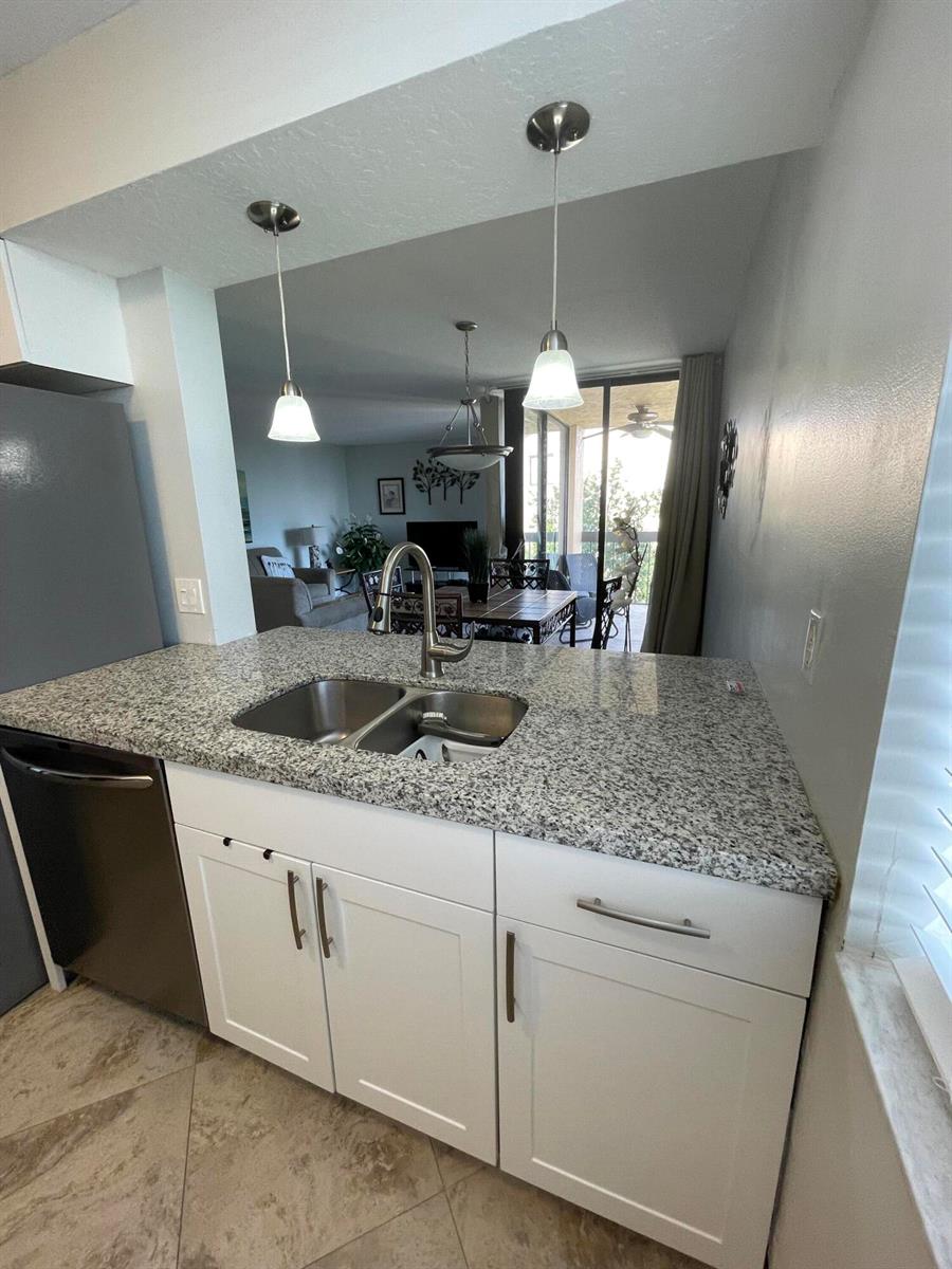 A kitchen features white cabinets, granite countertops, a stainless steel sink, and pendant lighting — 955 Dotterel Road # 2511, Delray Beach FL 33444, DELRAY BEACH, FL