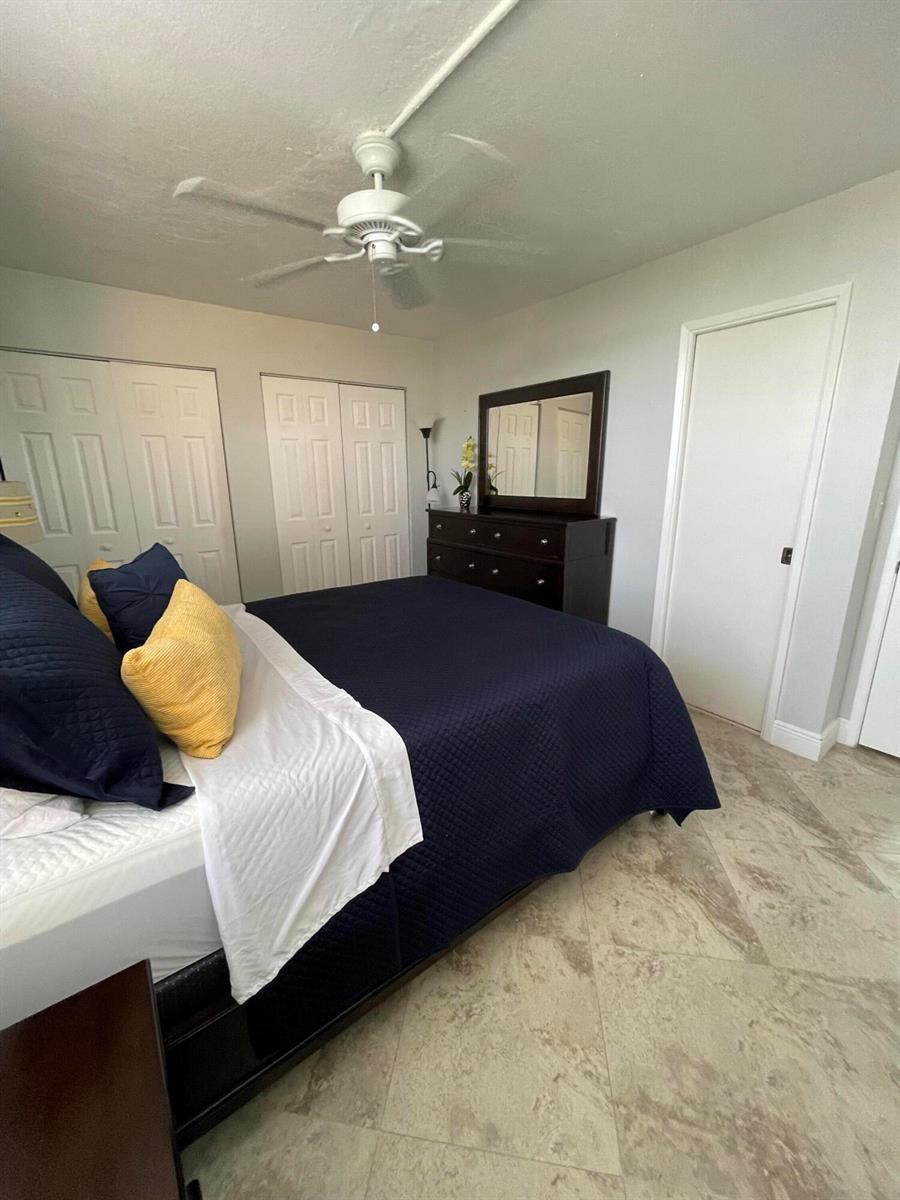 A bedroom features a dark blue bed, a wooden dresser with a mirror, and tile flooring — 955 Dotterel Road # 2511, Delray Beach FL 33444, DELRAY BEACH, FL
