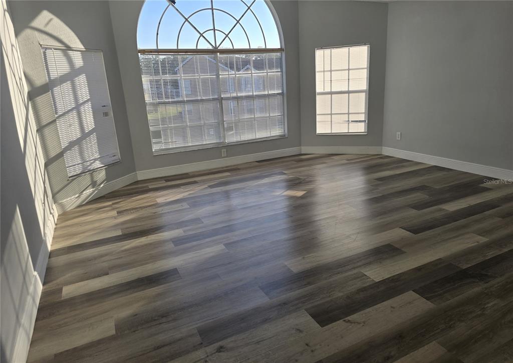 An empty room features light gray walls, wood-look plank flooring, and several windows — 2494 SWEETWATER CLUB CIRCLE UNIT 52, KISSIMMEE, FL