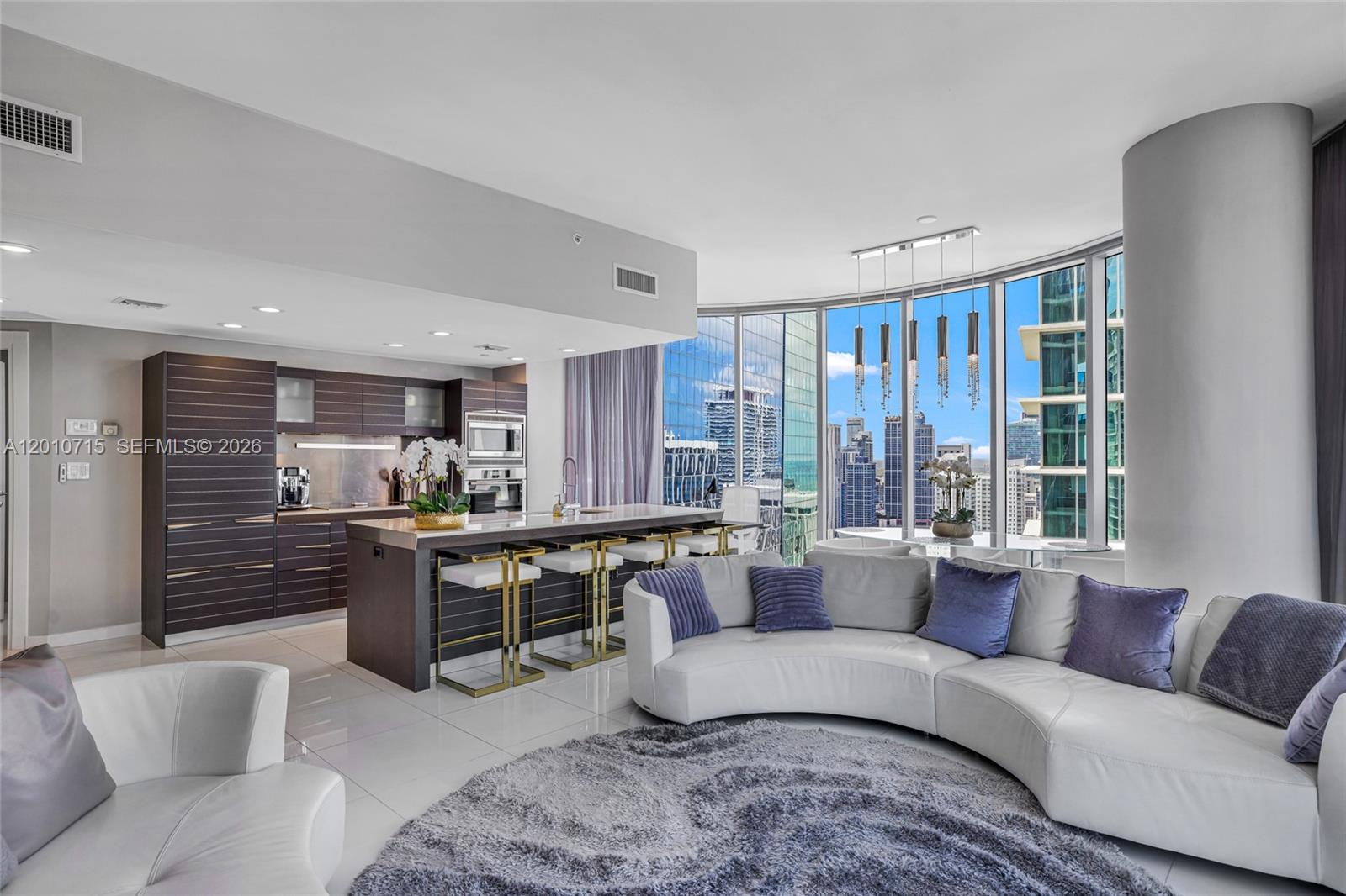 A modern living room features a curved sofa, circular rug, and floor-to-ceiling windows with city views — 200 Biscayne Boulevard Way # 4401, Miami FL 33131, MIAMI, FL