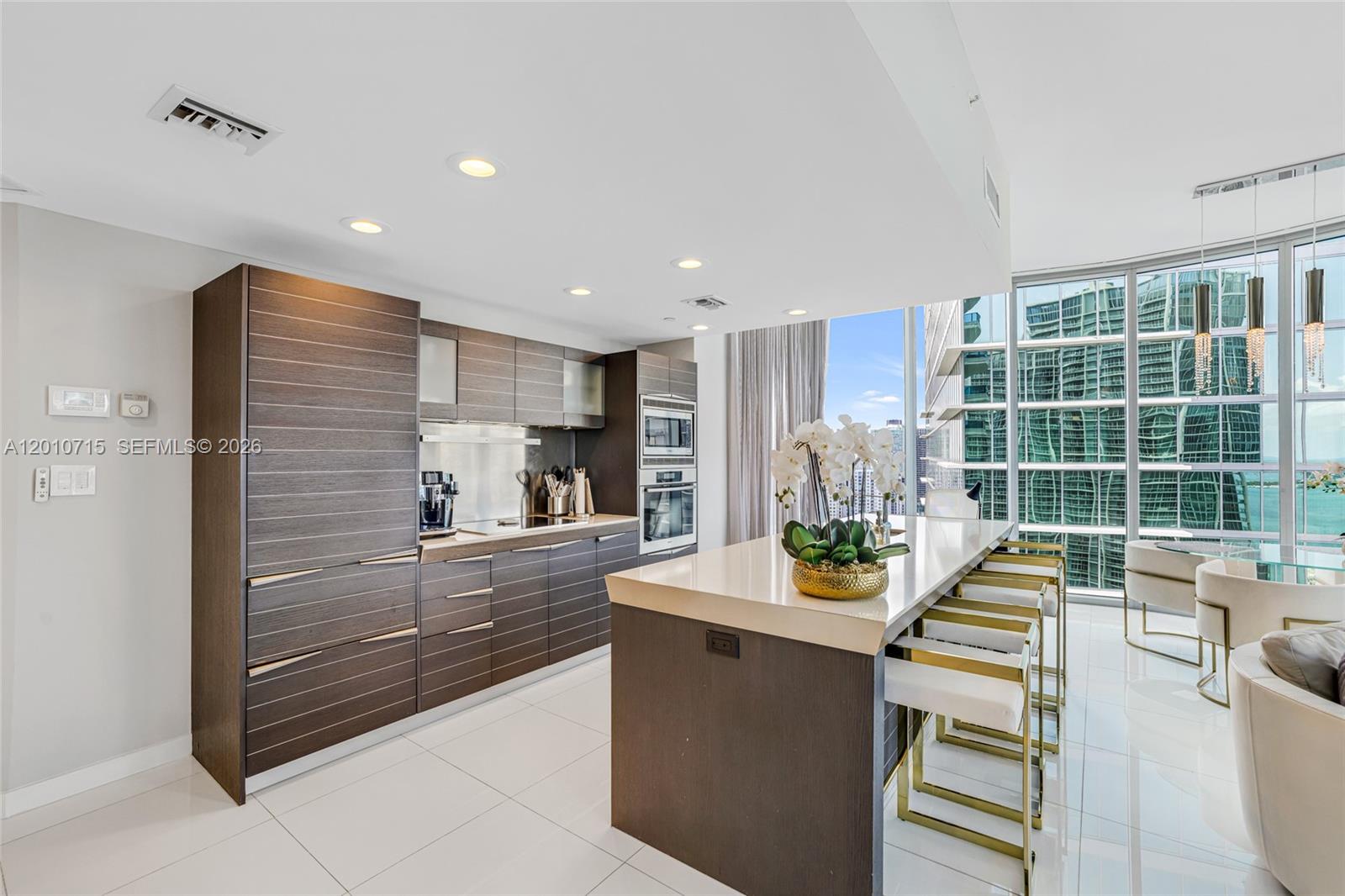 A modern kitchen features dark wood cabinetry, a large island, and floor-to-ceiling windows — 200 Biscayne Boulevard Way # 4401, Miami FL 33131, MIAMI, FL