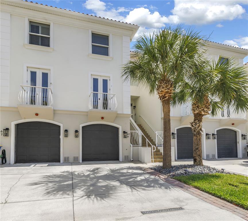 A multi-story townhouse exterior features gray garage doors, white balconies, and palm trees — 161 BRIGHTWATER DRIVE UNIT 6, CLEARWATER BEACH, FL