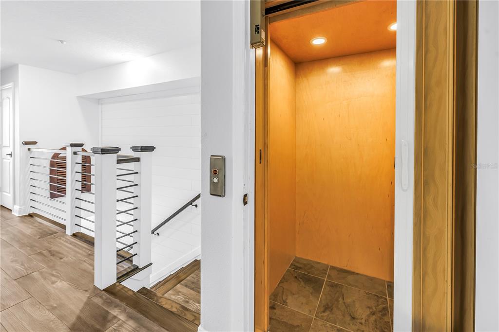 A home elevator with wood-paneled walls sits next to a staircase with white railings — 161 BRIGHTWATER DRIVE UNIT 6, CLEARWATER BEACH, FL