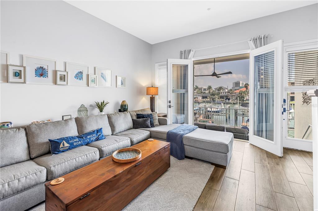 A living room features a gray sectional sofa, wooden coffee table, and doors opening to a balcony — 161 BRIGHTWATER DRIVE UNIT 6, CLEARWATER BEACH, FL