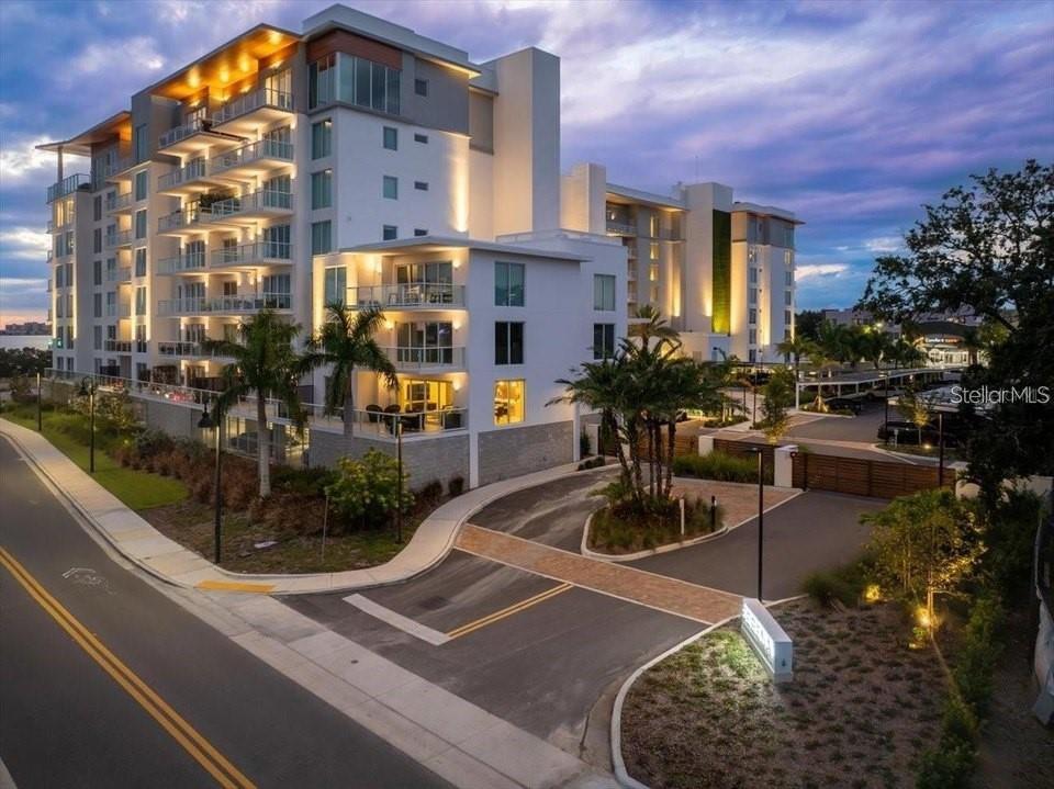 A multi-story modern apartment building with balconies and palm trees at dusk — 1020 SUNSET POINT ROAD UNIT 111, CLEARWATER, FL