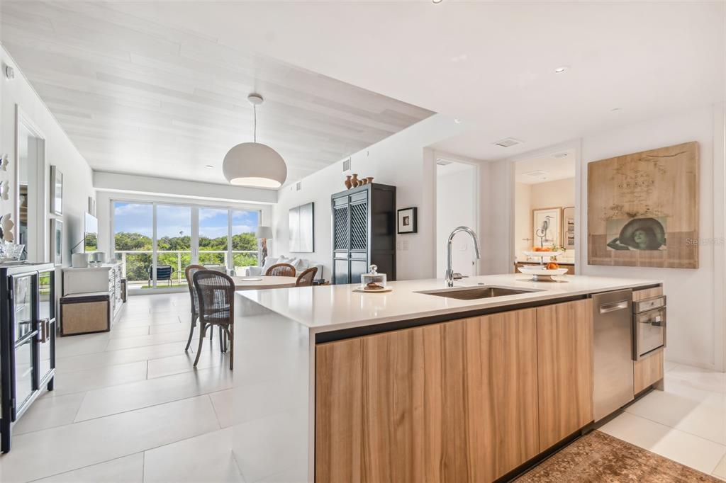 A modern kitchen with a wood-paneled island overlooks a dining area and a balcony — 1020 SUNSET POINT ROAD UNIT 111, CLEARWATER, FL