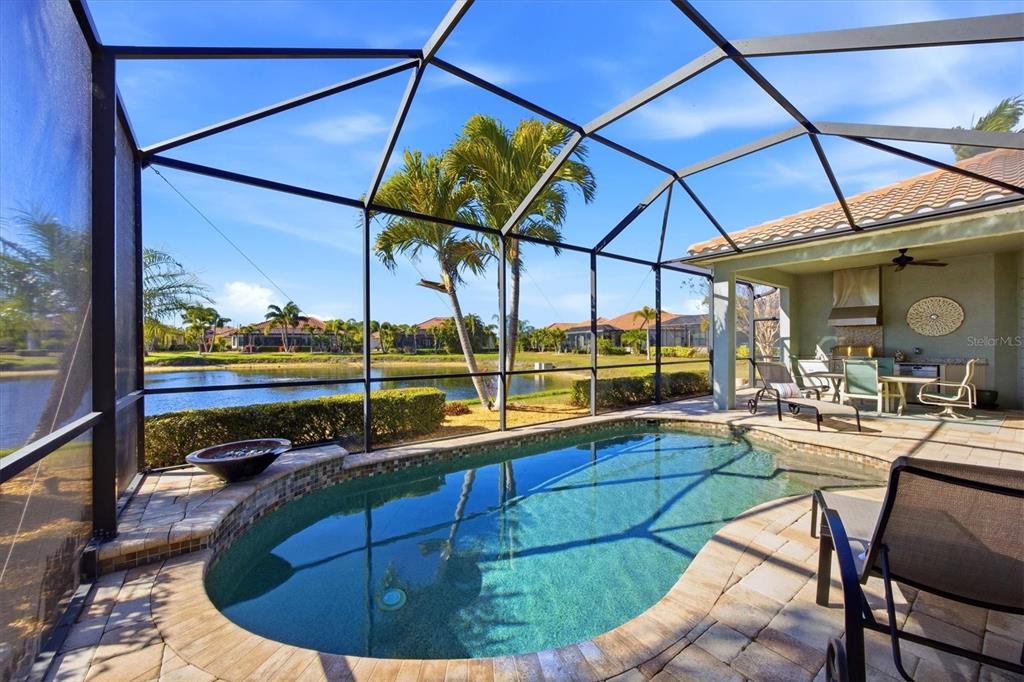 A screened-in pool patio features a small swimming pool, outdoor kitchen, and lake views — 20123 PASSAGIO DRIVE, VENICE, FL