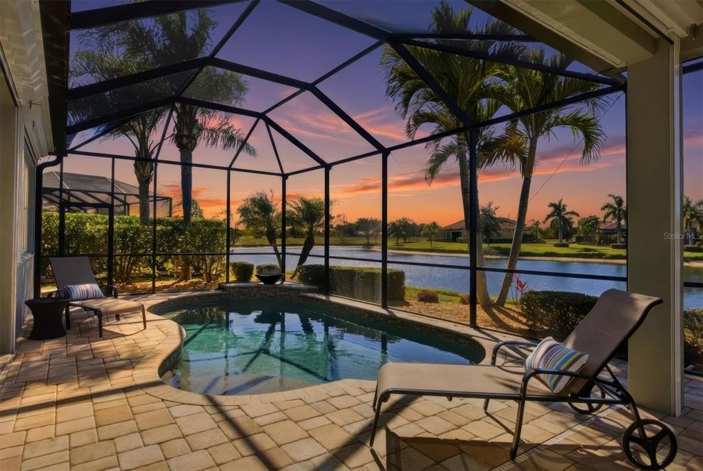A screened-in patio features a small swimming pool, lounge chairs, and a lake view — 20123 PASSAGIO DRIVE, VENICE, FL