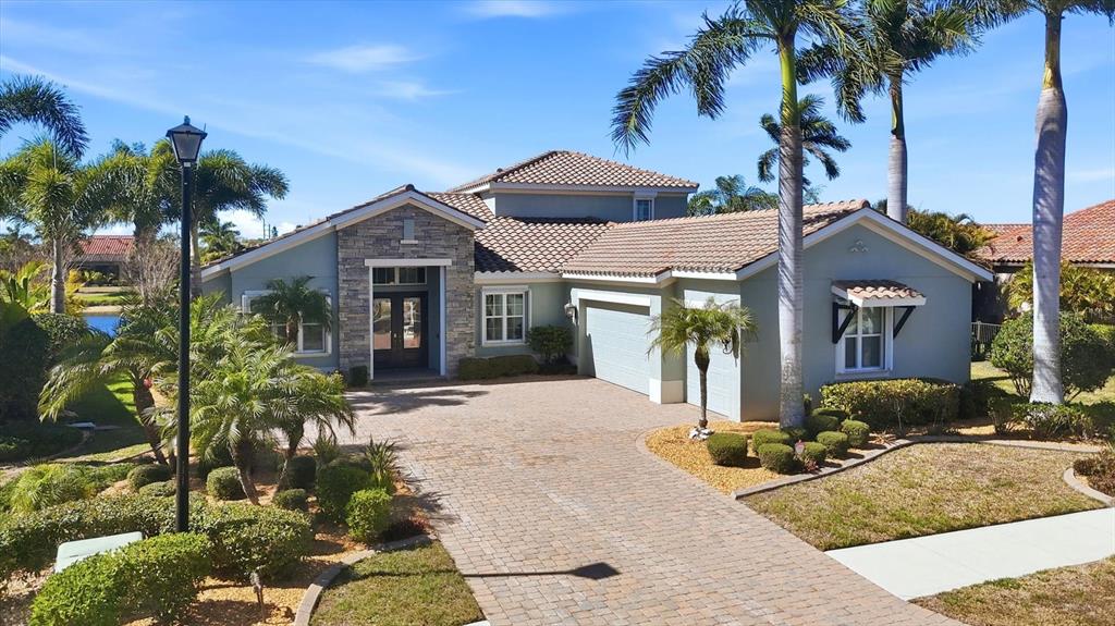 A single-story house with a stone facade, tile roof, and a paved driveway — 20123 PASSAGIO DRIVE, VENICE, FL