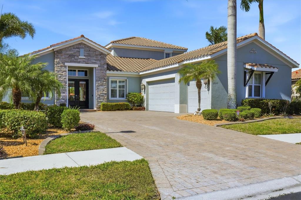 A single-story house with a stone-accented entryway, tiled roof, and a paved driveway — 20123 PASSAGIO DRIVE, VENICE, FL